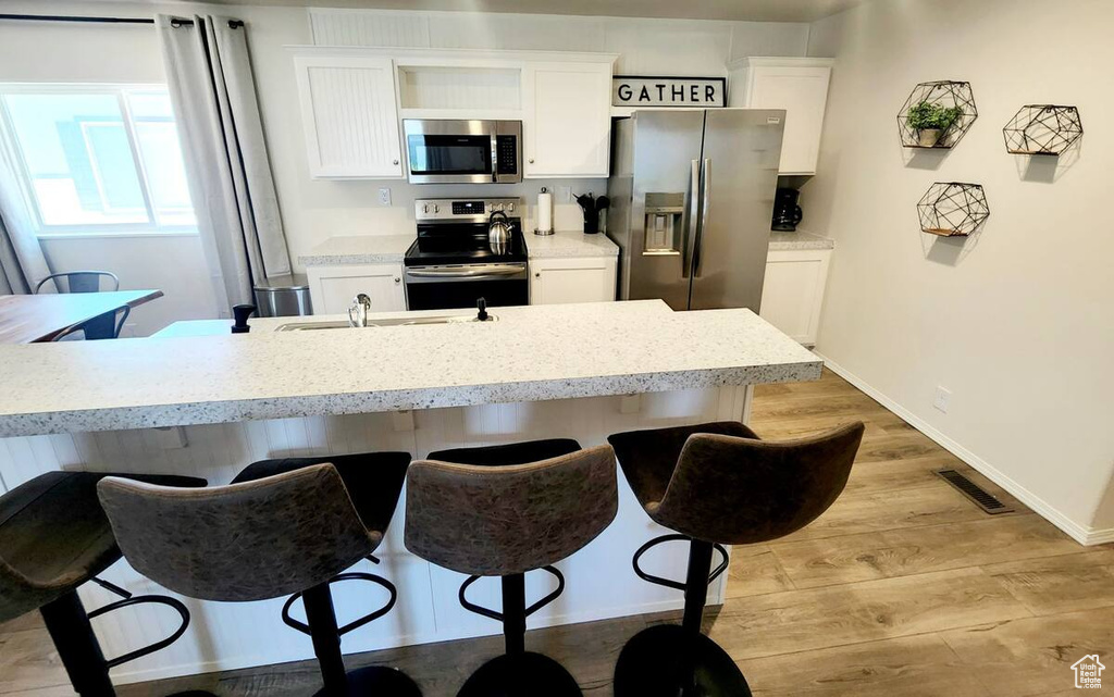 Kitchen with white cabinets, appliances with stainless steel finishes, a breakfast bar, and light wood-type flooring