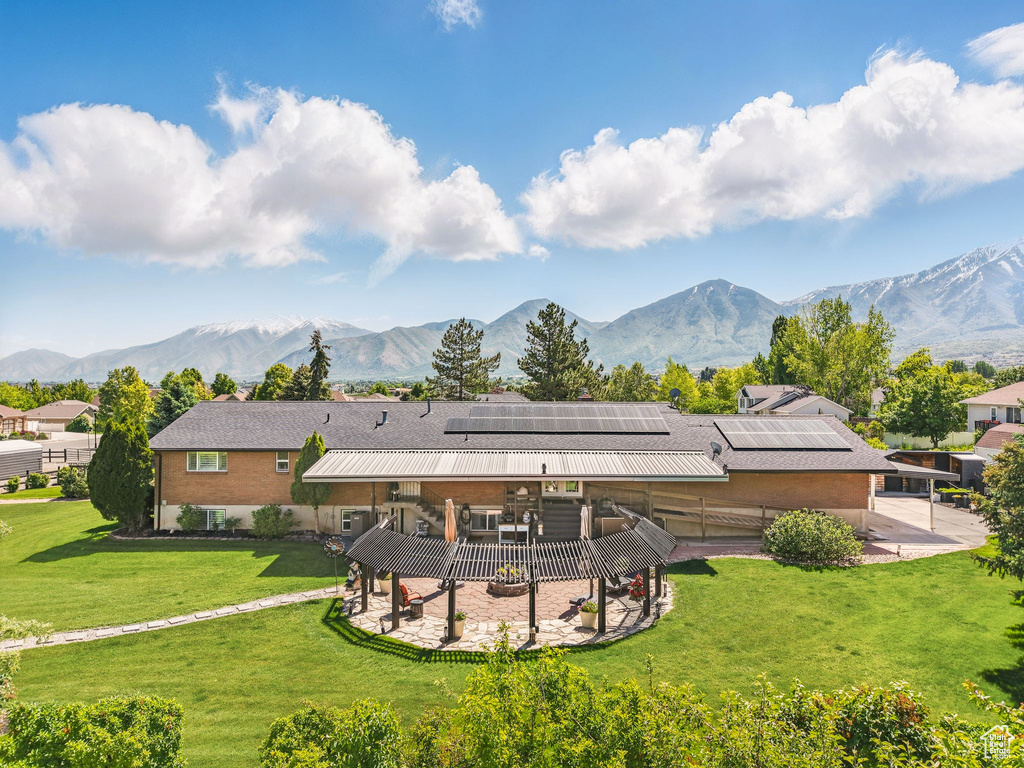Back of property with a patio, a deck with mountain view, solar panels, and a yard