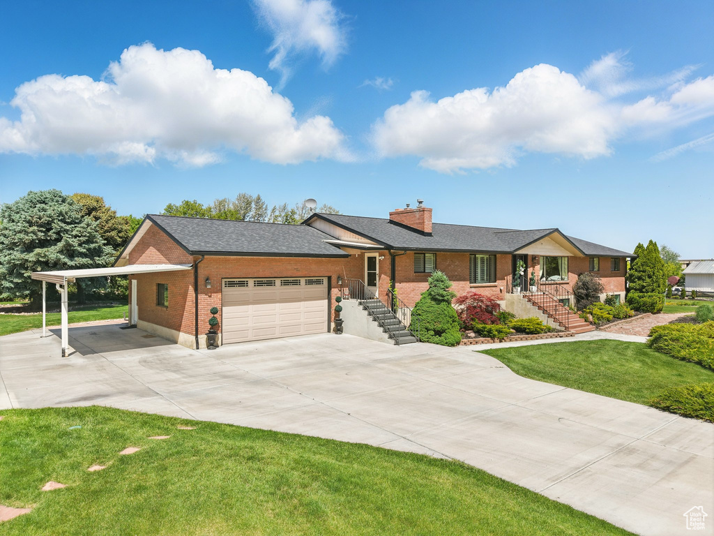 Single story home featuring brick siding, driveway, a chimney, an attached garage, and a front lawn