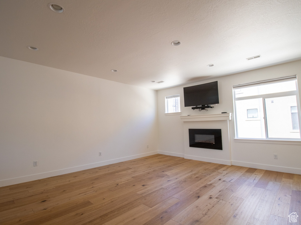 Unfurnished living room with light wood-style flooring, a glass covered fireplace, and recessed lighting