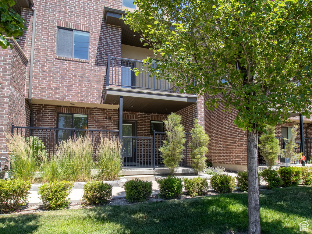 View of front of house with a balcony, brick siding, and a front yard