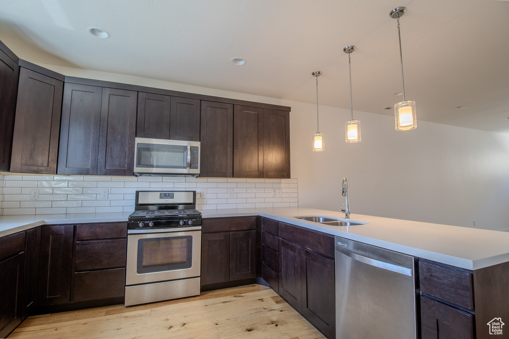 Kitchen with stainless steel appliances, light wood-style floors, a peninsula, backsplash, and dark brown cabinetry