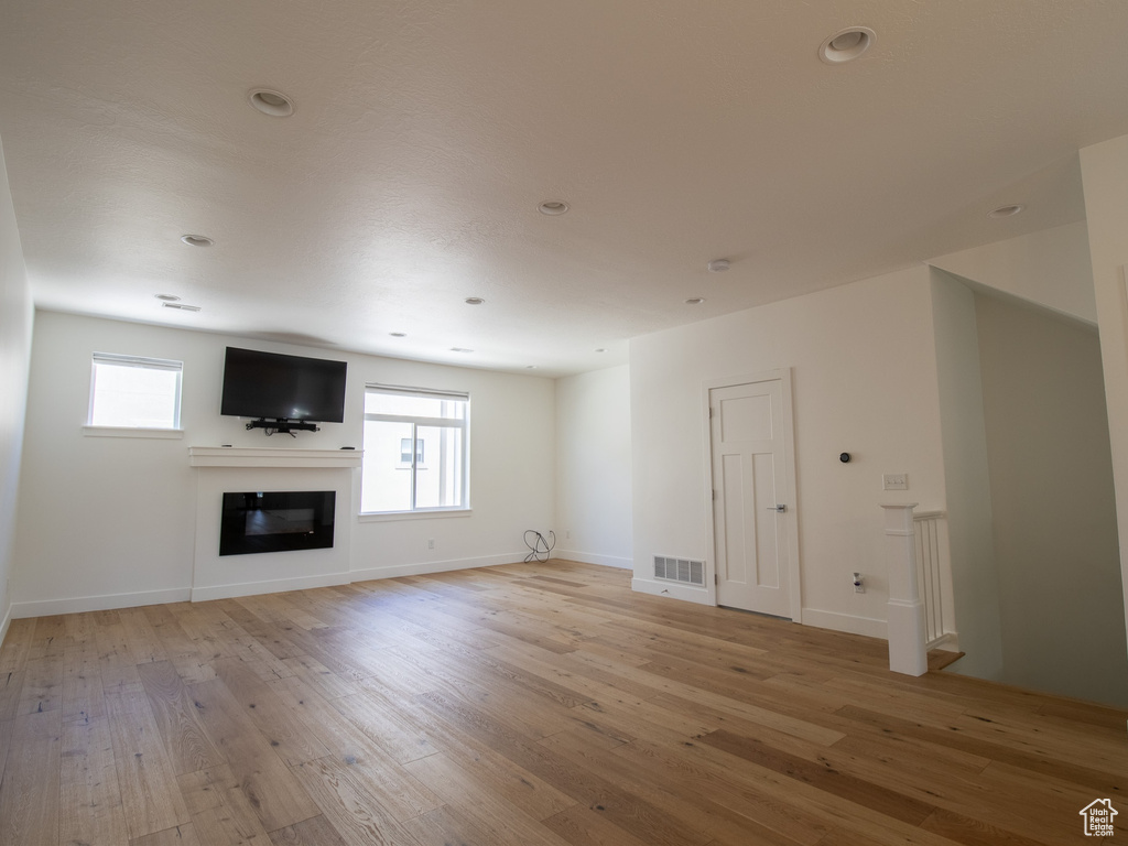 Unfurnished living room with light wood-style floors, a glass covered fireplace, and recessed lighting