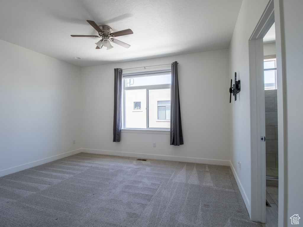 Carpeted empty room with a ceiling fan and plenty of natural light