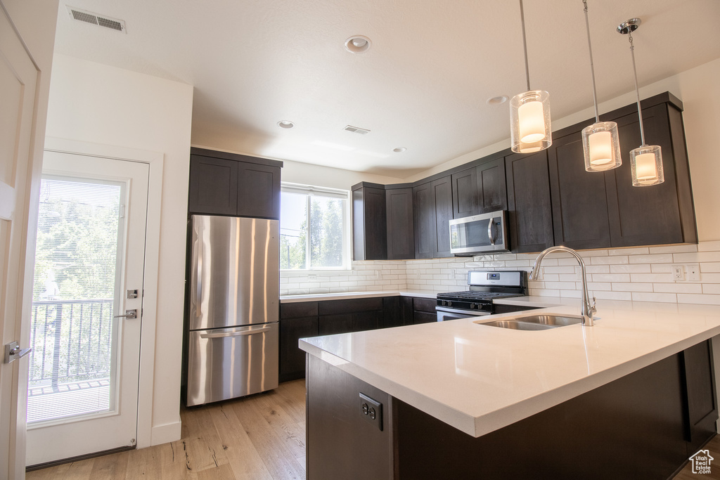Kitchen featuring stainless steel appliances, a peninsula, light wood finished floors, light countertops, and backsplash