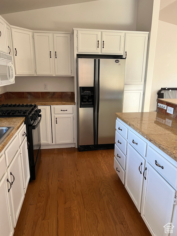 Kitchen with light stone countertops, stainless steel refrigerator with ice dispenser, black gas range oven, white cabinets, and dark hardwood / wood-style floors