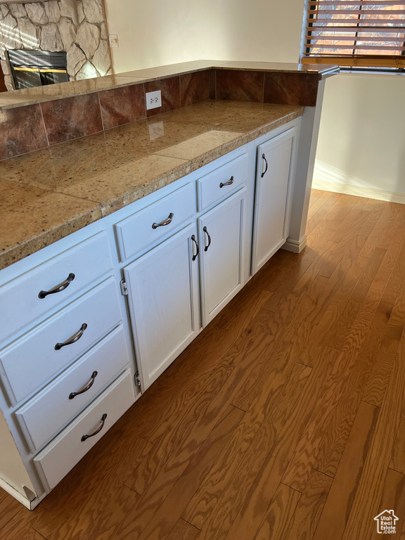 Kitchen featuring light hardwood / wood-style floors, light stone countertops, white cabinetry, and a stone fireplace