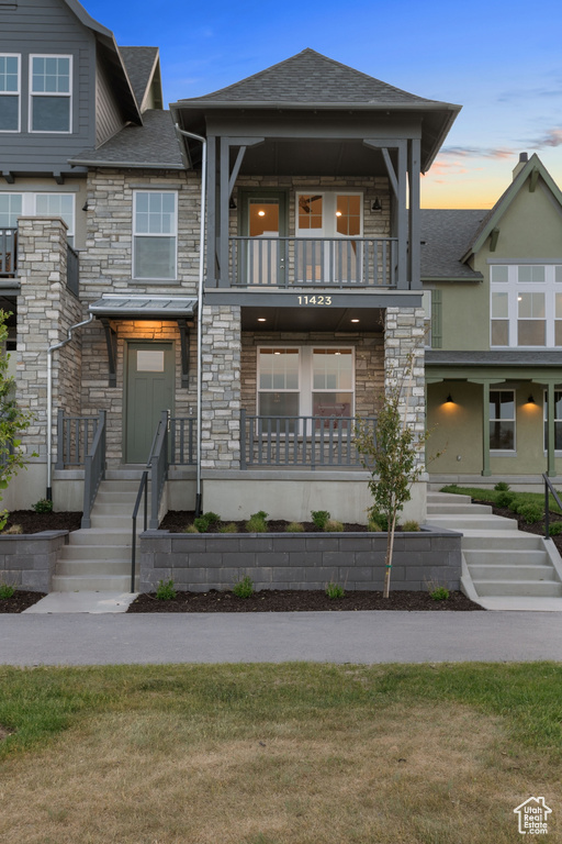 View of front facade featuring a balcony, stone siding, roof with shingles, and stairway