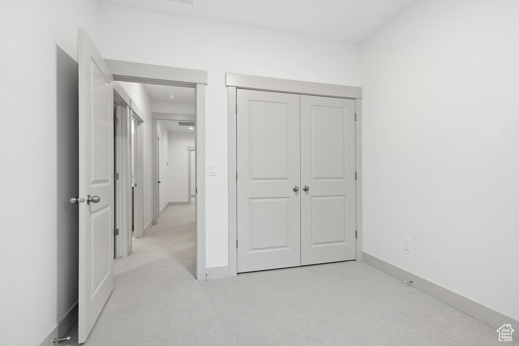 Unfurnished bedroom featuring light carpet, a closet, and baseboards