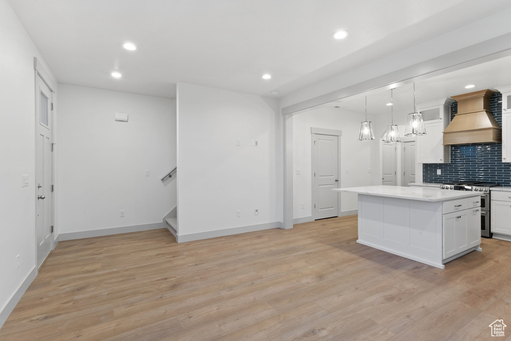 Kitchen with stainless steel gas range oven, custom range hood, backsplash, white cabinets, and recessed lighting