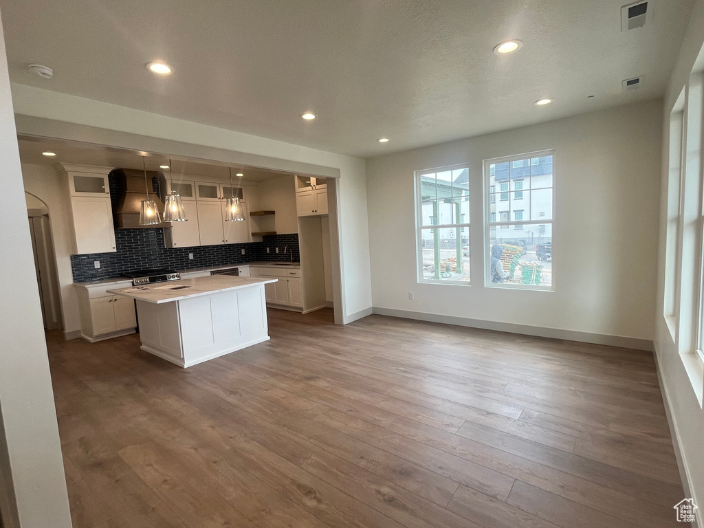 Kitchen featuring tasteful backsplash, visible vents, white cabinets, baseboards, and wall chimney exhaust hood