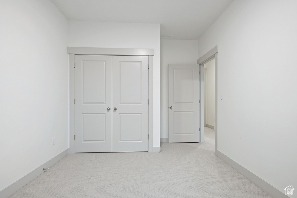 Unfurnished bedroom with light carpet, baseboards, and a closet