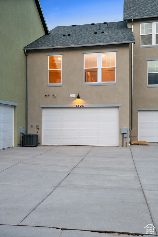 Back of property with stucco siding, an attached garage, roof with shingles, and driveway