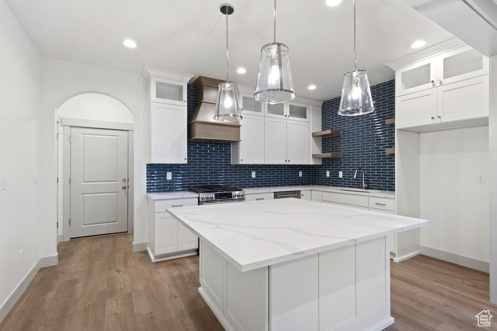 Kitchen featuring custom exhaust hood, open shelves, a sink, stainless steel appliances, and tasteful backsplash