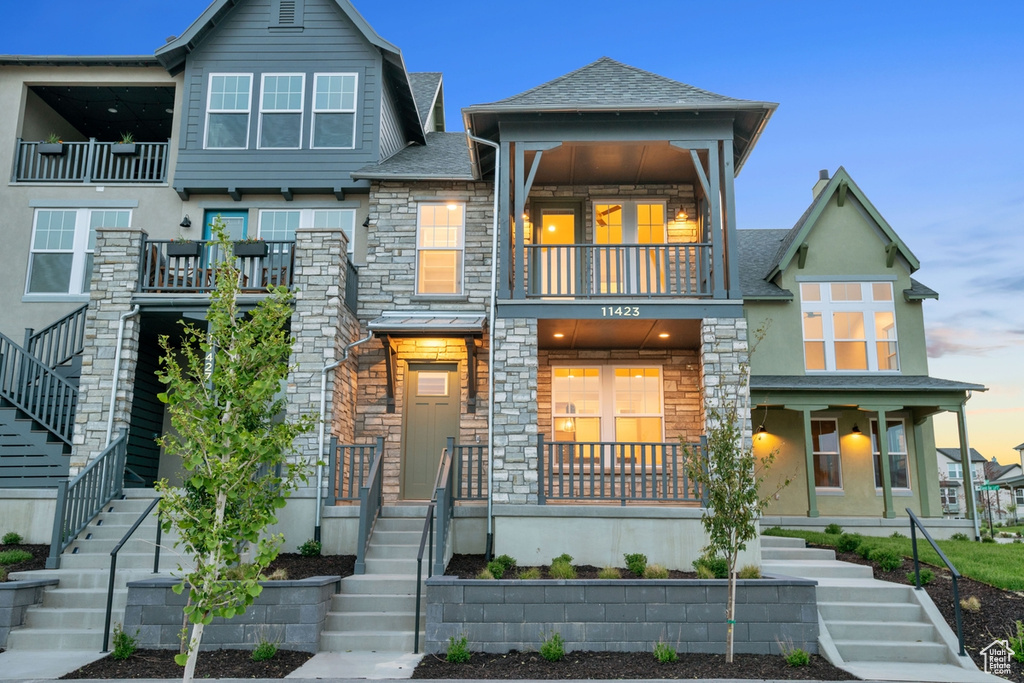 View of front of house featuring stairway, a balcony, stone siding, and stucco siding