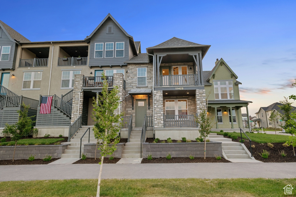 View of front of home with stone siding, stairs, a balcony, and stucco siding