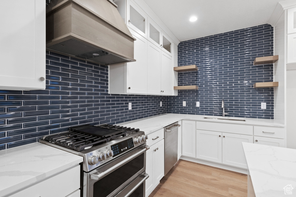 Kitchen with open shelves, stainless steel appliances, a sink, premium range hood, and tasteful backsplash