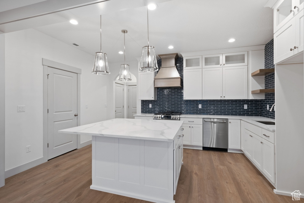 Kitchen featuring dishwasher, custom exhaust hood, a sink, light wood finished floors, and backsplash