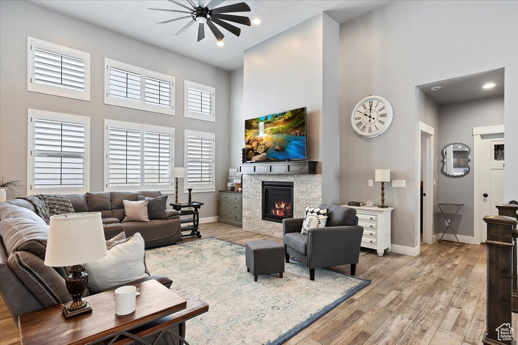 Living area featuring a high ceiling, a glass covered fireplace, ceiling fan, light wood-style floors, and baseboards