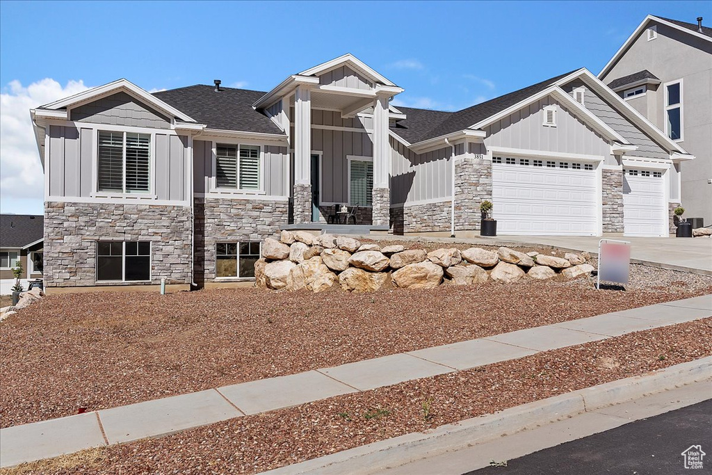 Craftsman house featuring board and batten siding, stone siding, a garage, driveway, and roof with shingles