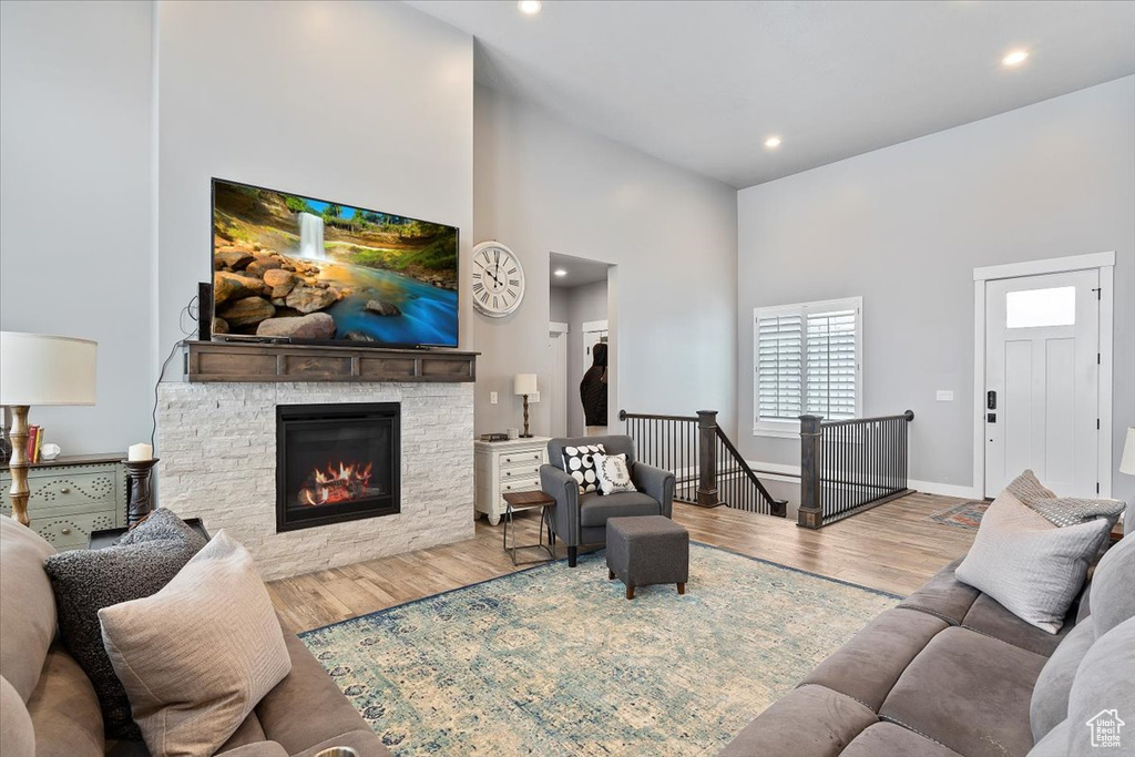 Living area with a high ceiling, a stone fireplace, wood finished floors, recessed lighting, and baseboards