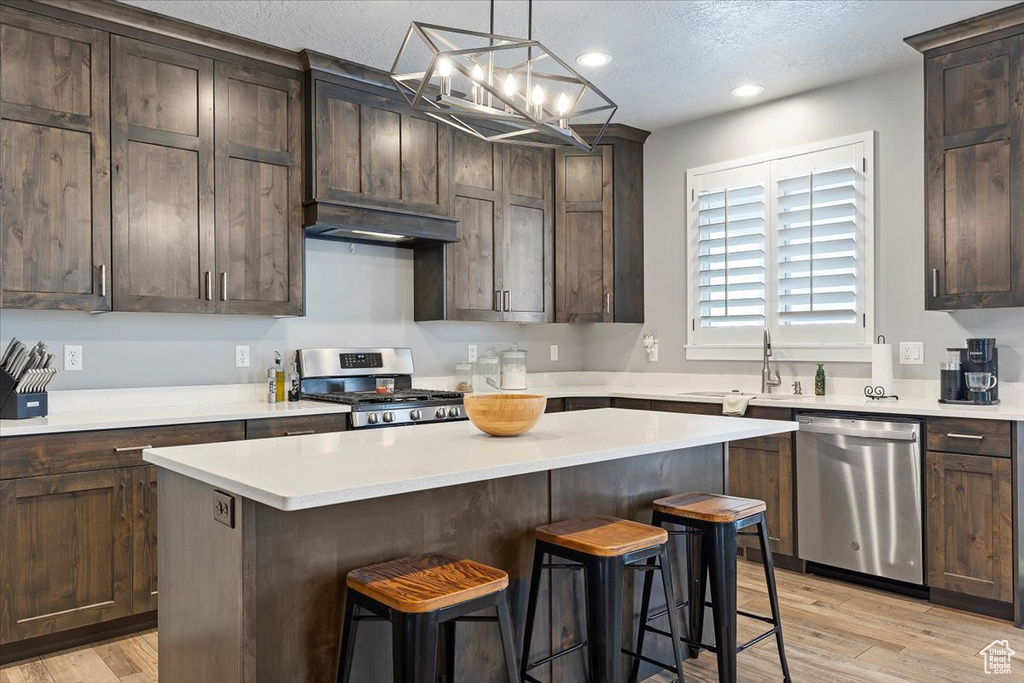 Kitchen with appliances with stainless steel finishes, a sink, a kitchen breakfast bar, light countertops, and a center island