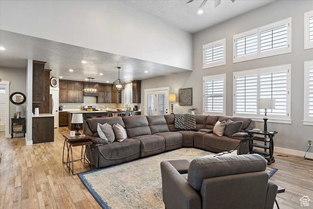 Living room with baseboards, light wood-type flooring, a towering ceiling, recessed lighting, and plenty of natural light