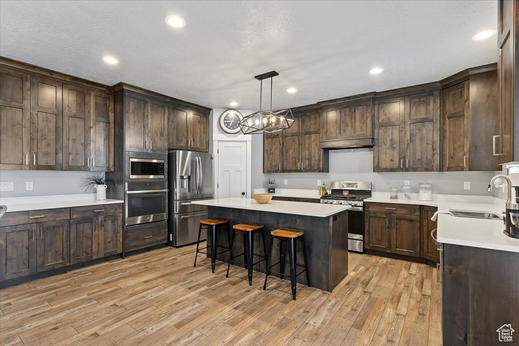 Kitchen featuring appliances with stainless steel finishes, a sink, under cabinet range hood, a center island, and a breakfast bar