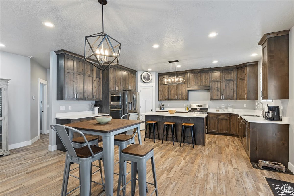 Kitchen with a sink, a kitchen island, dark brown cabinets, appliances with stainless steel finishes, and light wood-style floors
