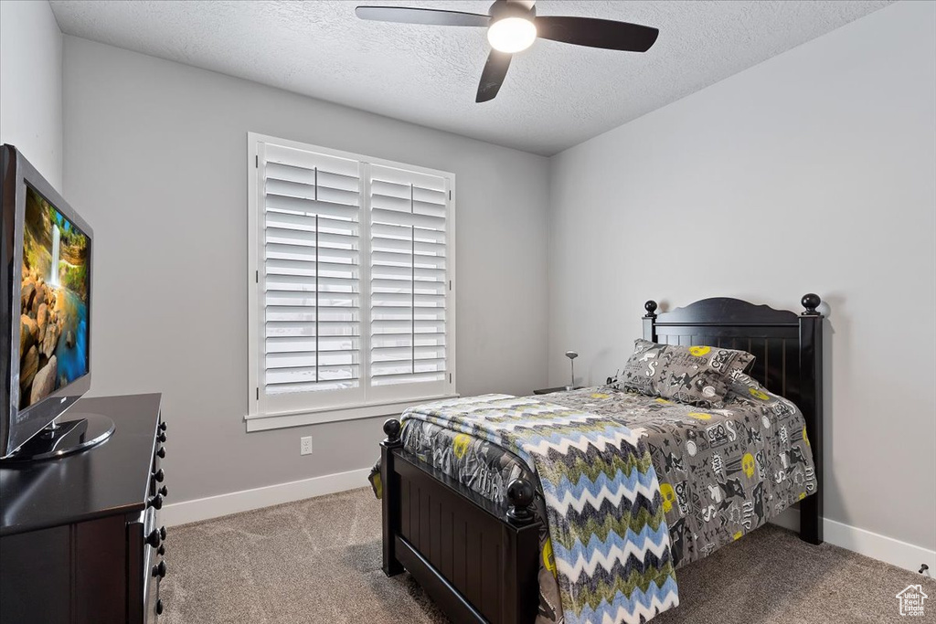 Carpeted bedroom featuring a textured ceiling, ceiling fan, and baseboards