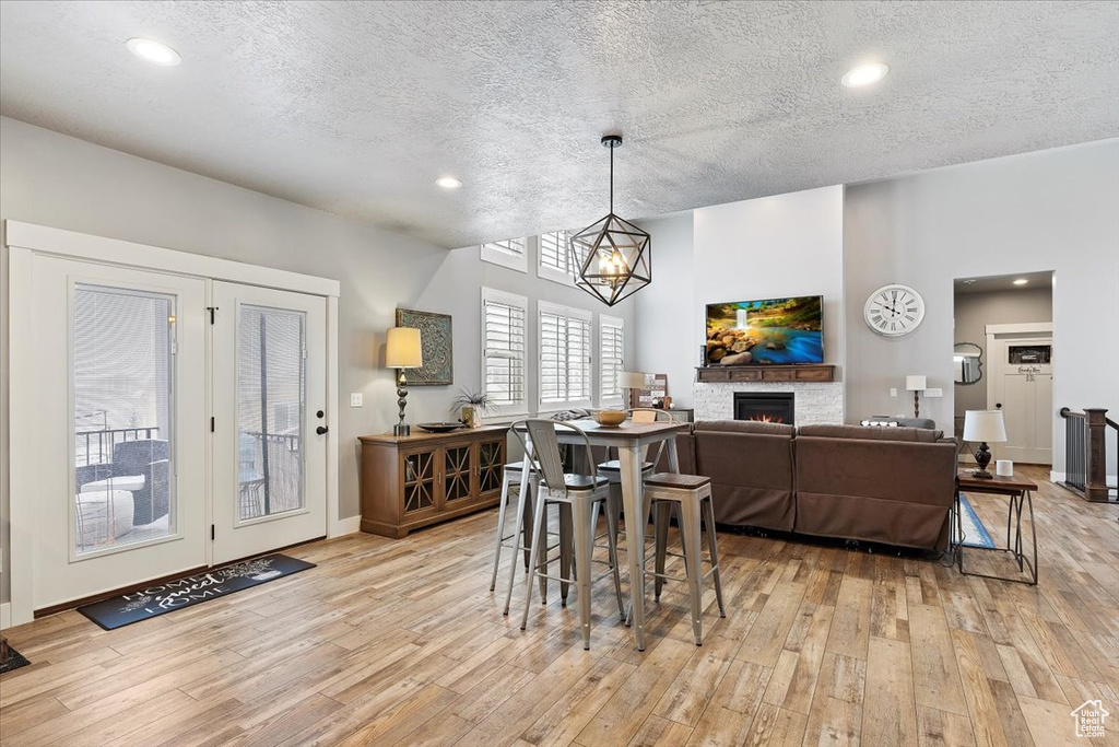 Dining room featuring light wood-type flooring, a warm lit fireplace, a textured ceiling, a chandelier, and recessed lighting