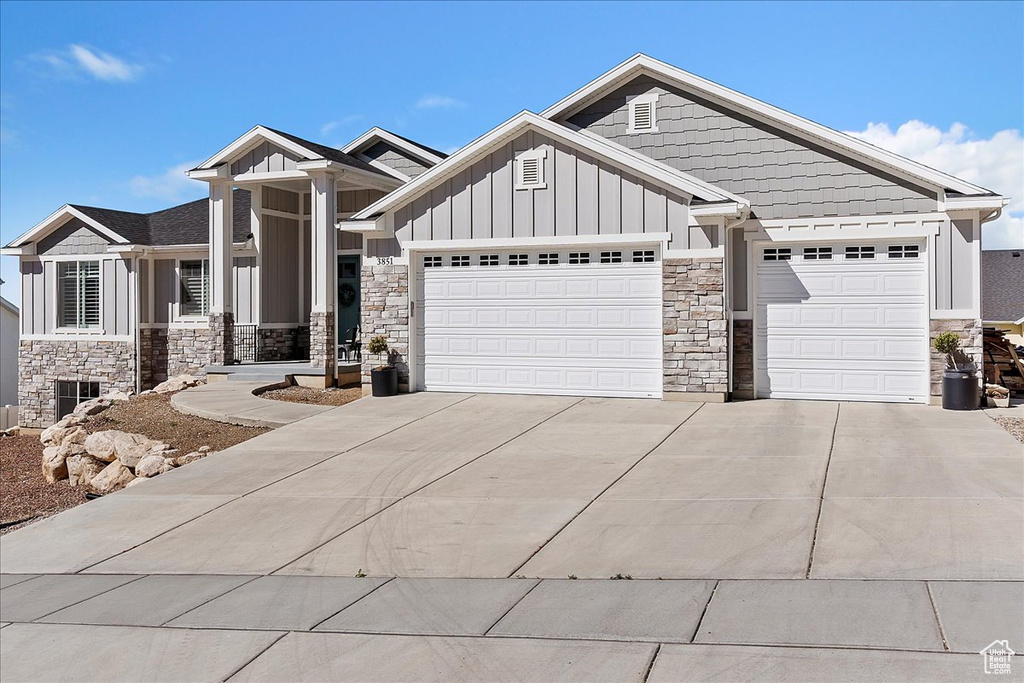 Craftsman inspired home featuring board and batten siding, stone siding, a garage, and driveway