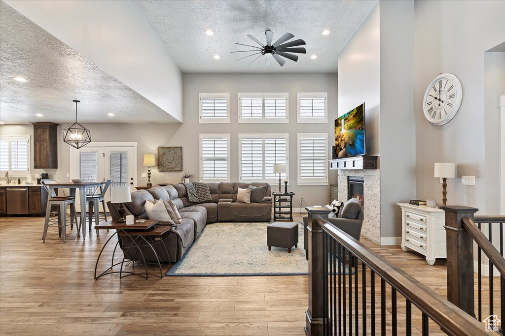 Living area with a textured ceiling, a ceiling fan, recessed lighting, a towering ceiling, and a stone fireplace