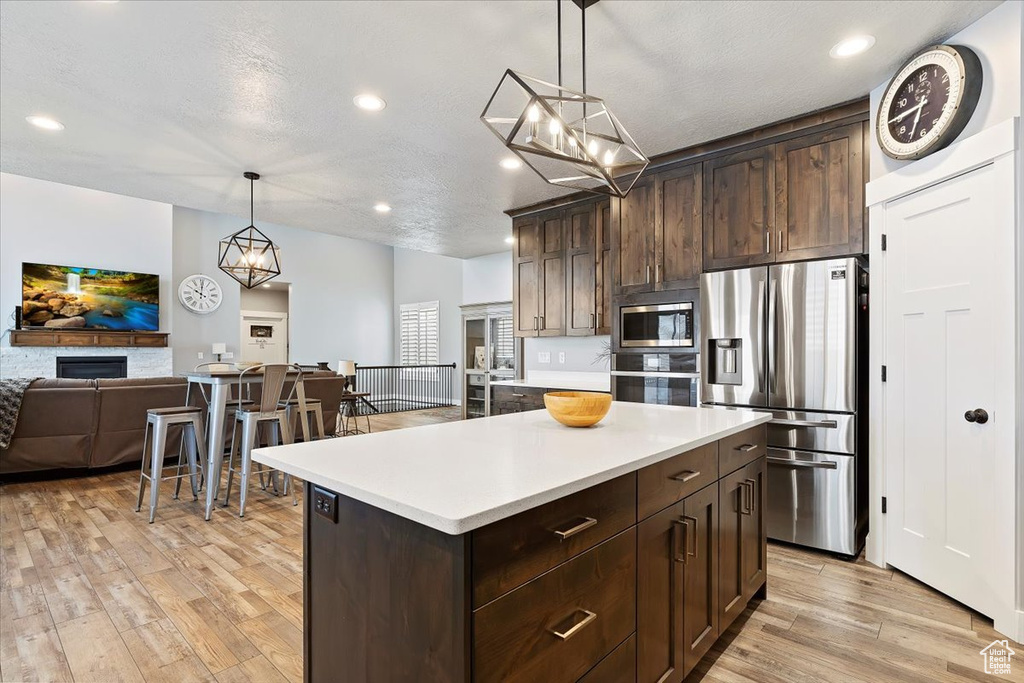 Kitchen with stainless steel appliances, open floor plan, light wood-style flooring, dark brown cabinets, and light countertops