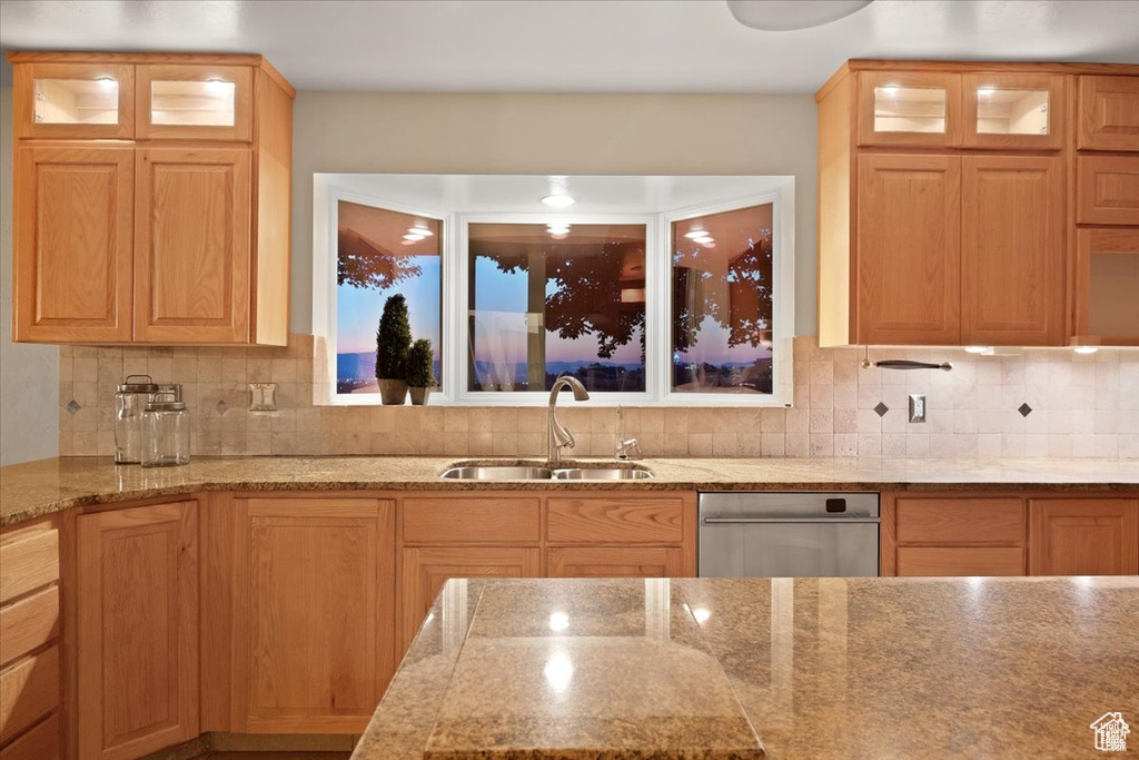 Kitchen featuring dishwasher, light stone counters, sink, and tasteful backsplash