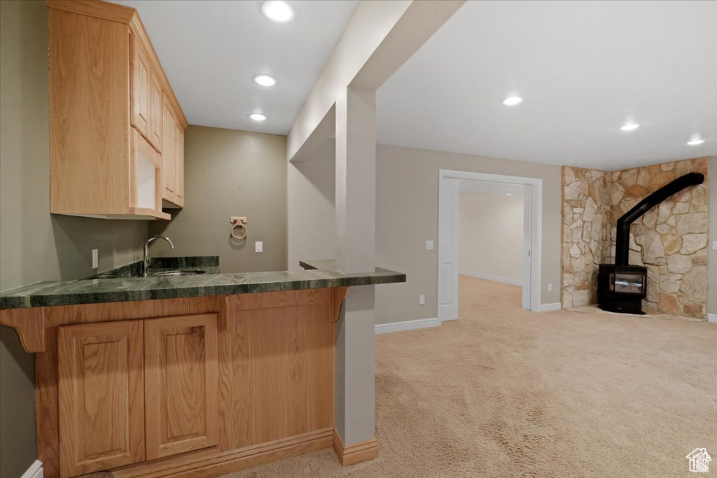 Bar featuring light brown cabinetry, a wood stove, sink, and light colored carpet