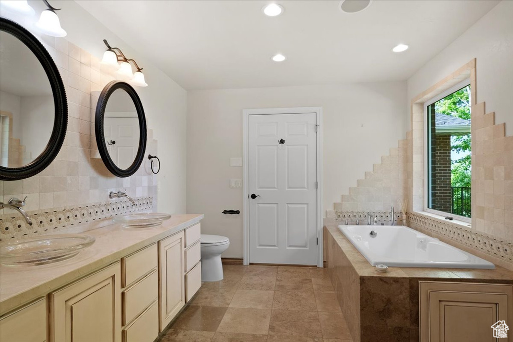 Bathroom featuring backsplash, tile patterned floors, vanity, tiled bath, and toilet
