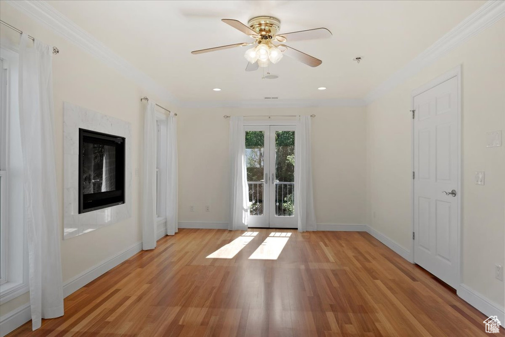 Unfurnished room with french doors, light wood-type flooring, ceiling fan, crown molding, and a fireplace