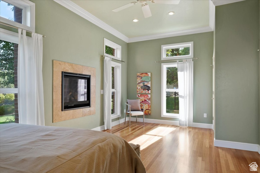 Bedroom with a tile fireplace, light hardwood / wood-style flooring, multiple windows, and ceiling fan