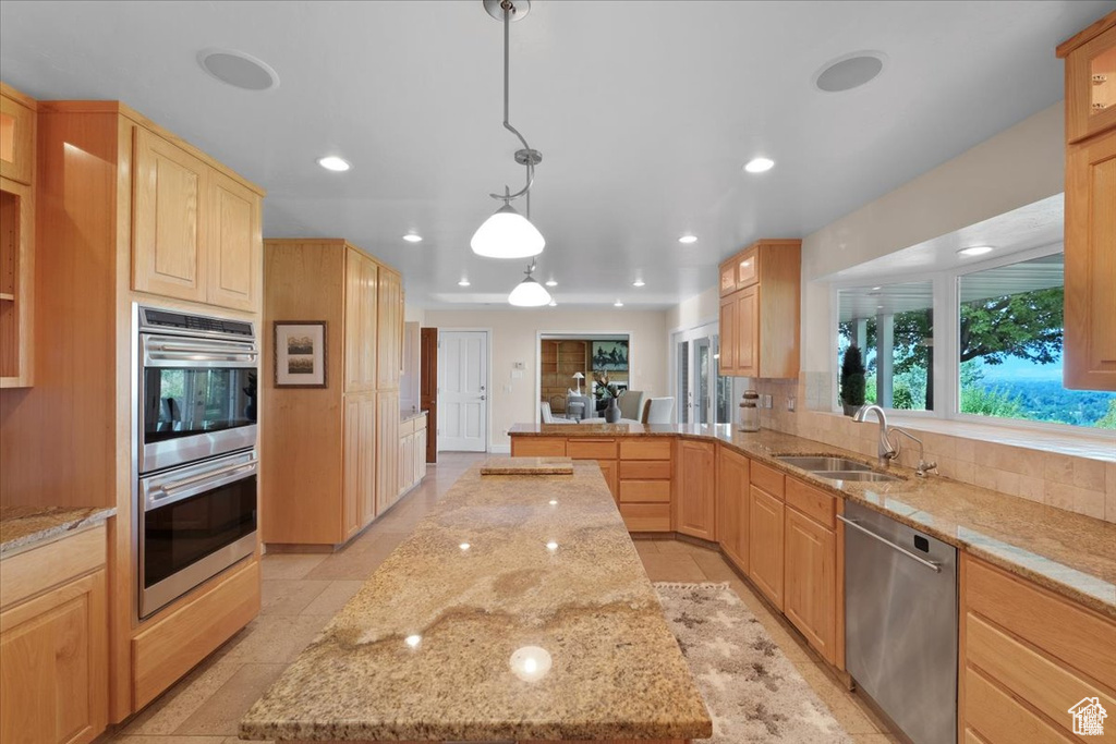 Kitchen featuring light stone countertops, stainless steel appliances, sink, light brown cabinets, and decorative light fixtures