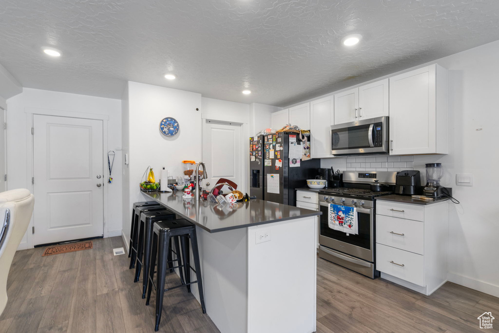 Kitchen featuring kitchen peninsula, appliances with stainless steel finishes, dark hardwood / wood-style flooring, white cabinetry, and a breakfast bar area