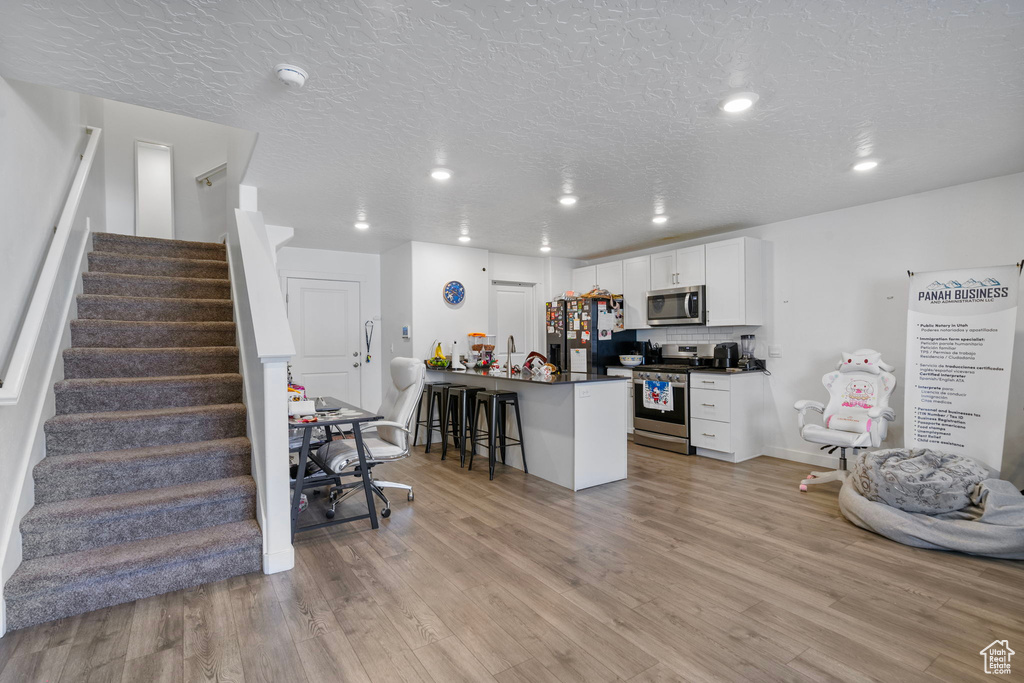 Kitchen with light hardwood / wood-style flooring, a textured ceiling, a breakfast bar, white cabinets, and appliances with stainless steel finishes