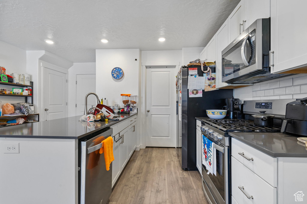 Kitchen featuring white cabinets, light wood-type flooring, a textured ceiling, and appliances with stainless steel finishes