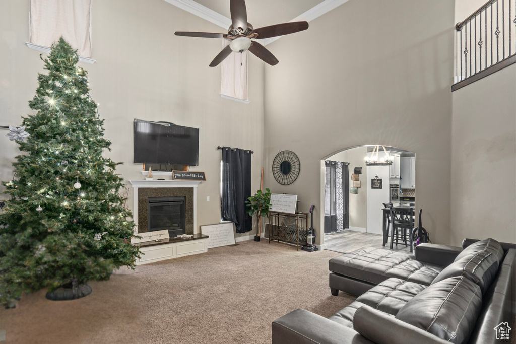 Carpeted living room featuring ceiling fan with notable chandelier, a towering ceiling, and crown molding