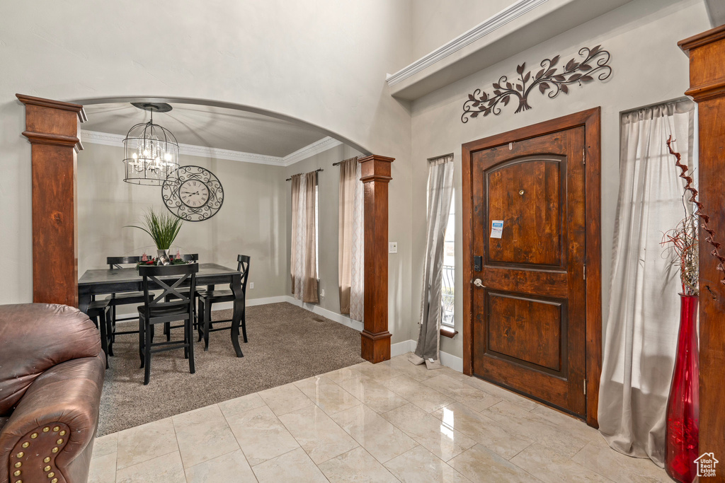 Carpeted foyer with ornate columns, crown molding, and an inviting chandelier