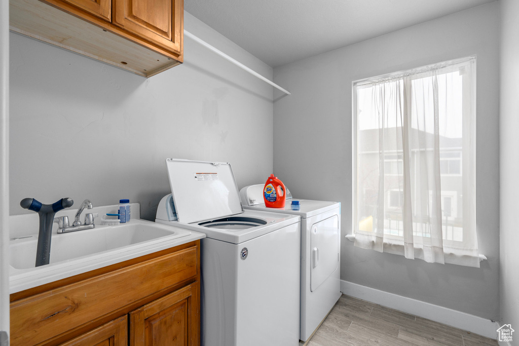 Laundry area with washing machine and clothes dryer, sink, cabinets, and light wood-type flooring