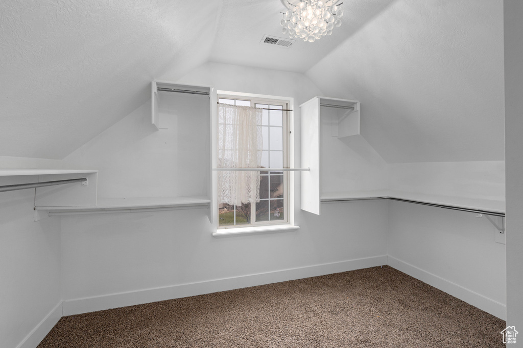 Spacious closet with carpet flooring, an inviting chandelier, and vaulted ceiling