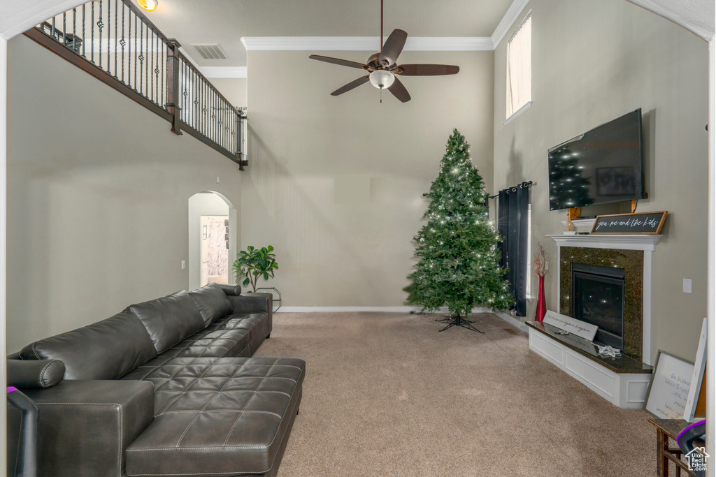 Carpeted living room featuring ceiling fan, a premium fireplace, a towering ceiling, and ornamental molding