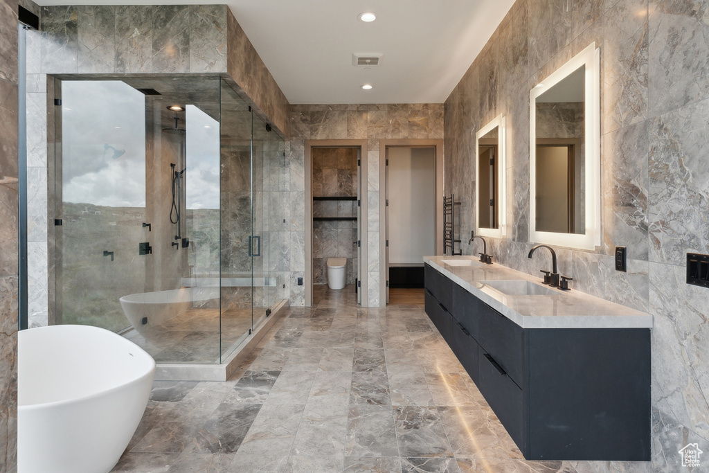 Bathroom with double vanity, a freestanding tub, marble tiled floors, a shower stall, and tile walls