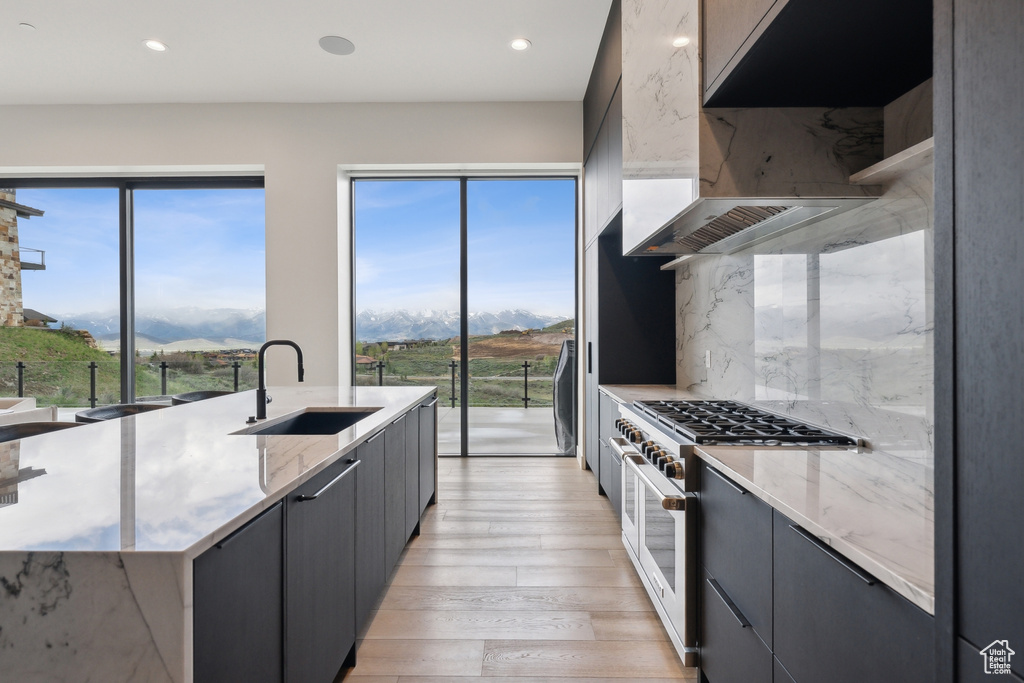 Kitchen with high end stainless steel range, a sink, light wood-style floors, light stone countertops, and recessed lighting